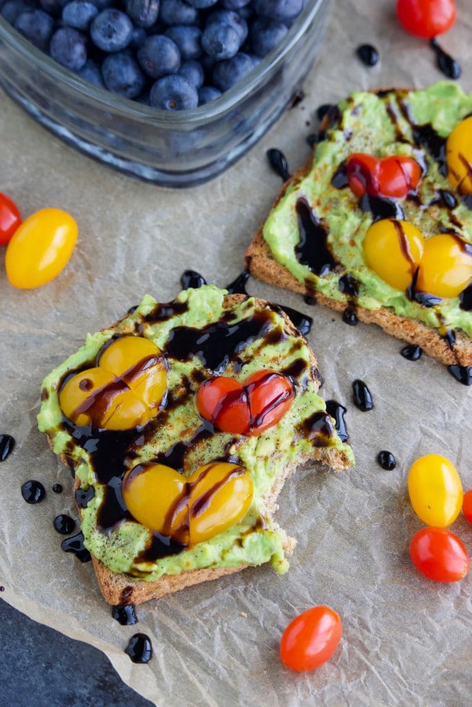 Two slices of bread, one with a bite taken out of it next to blueberries on a piece of parchment paper.