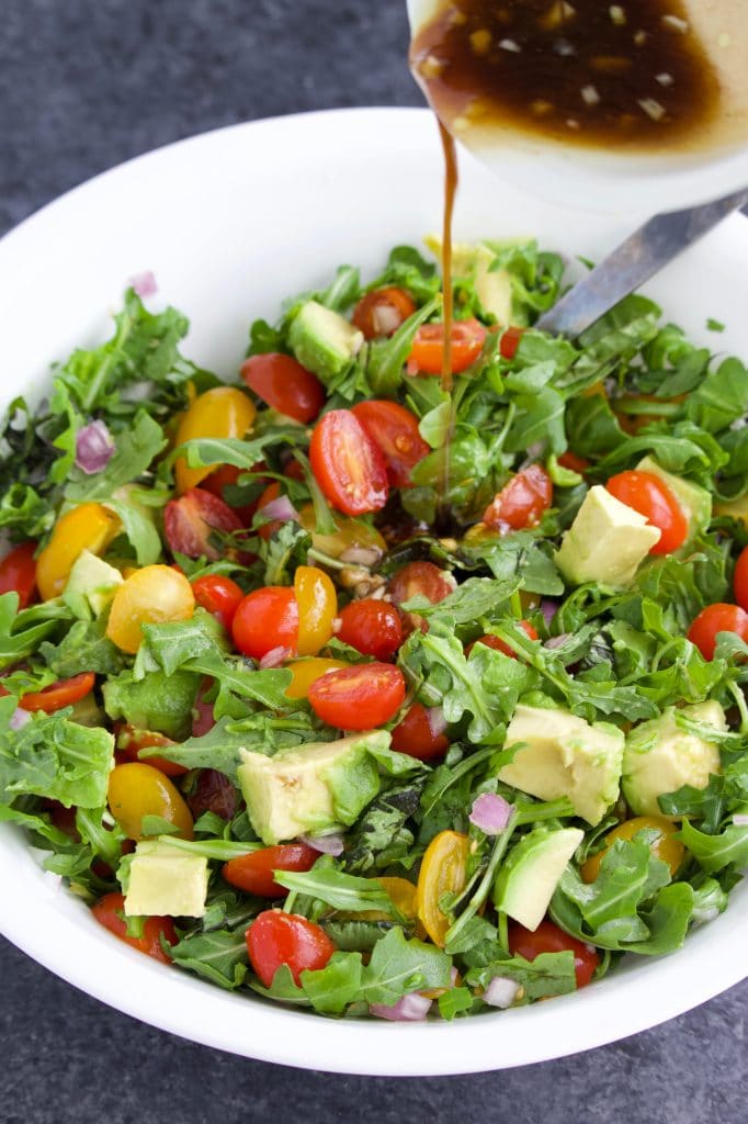 A small bowl pouring dressing into a large white bowl filled with salad.