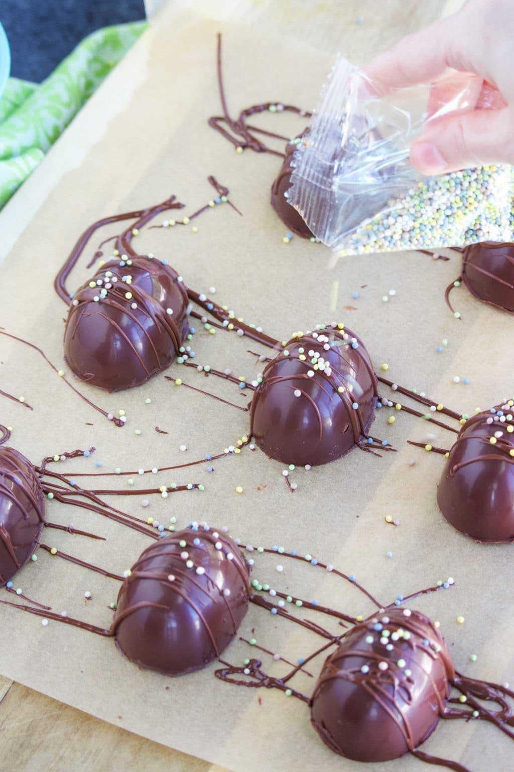 A hand putting sprinkles on chocolate eggs on top of parchment paper.