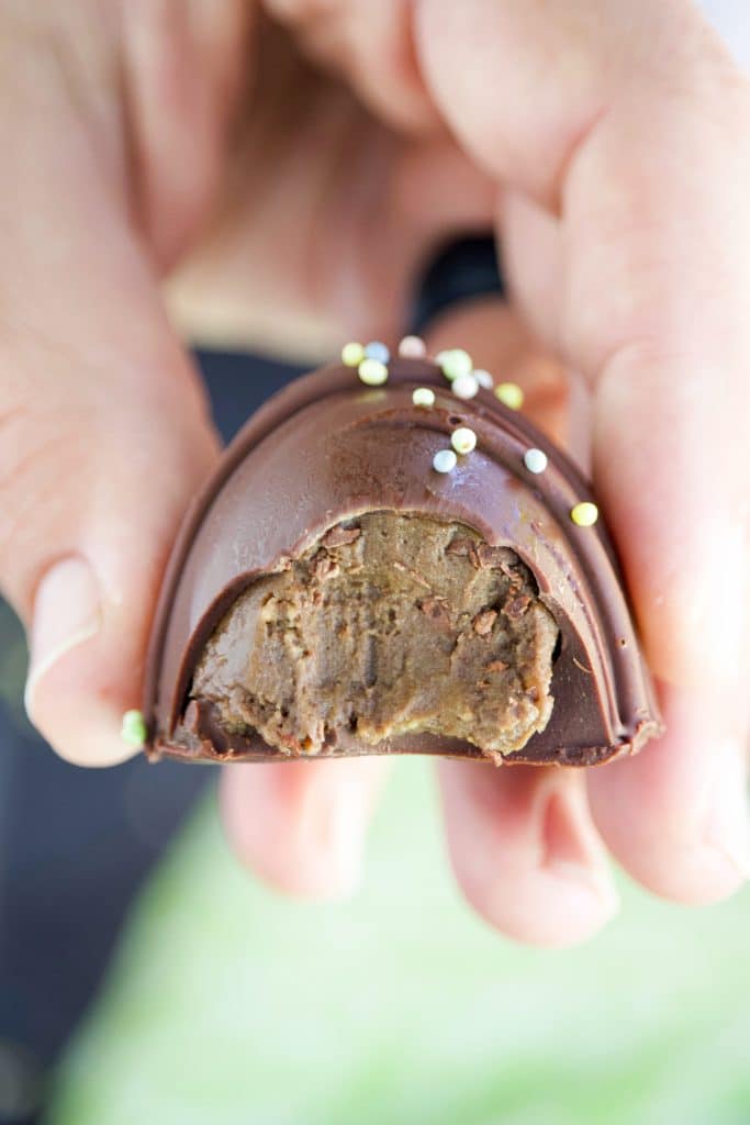A hand holding a chocolate egg that has a bite missing.