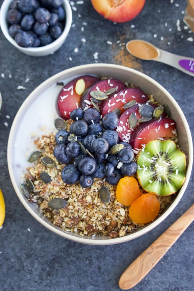 A white bowl filled with raw granola and fresh fruit on a dark background.