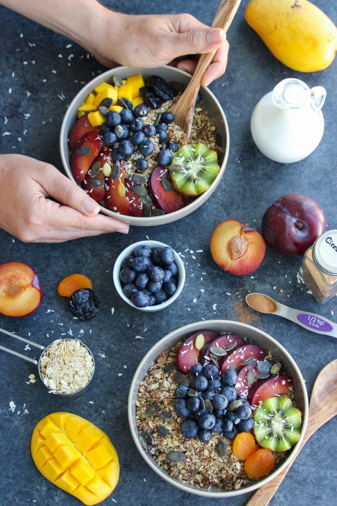 One bowl being held with two hands next to two other white bowls on a dark background.