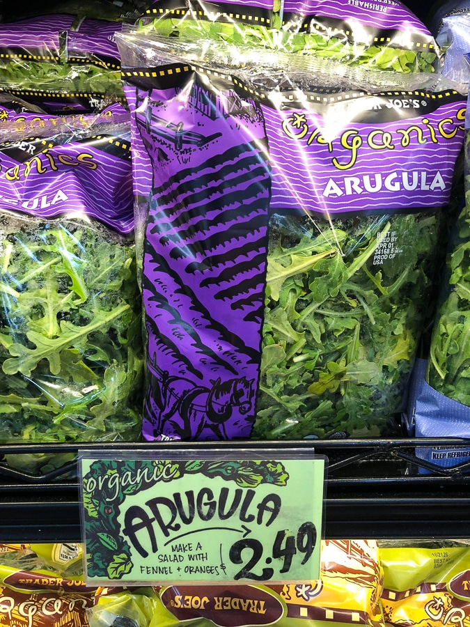 Multiple bags or organic arugula on a shelf at Trader Joe's. 