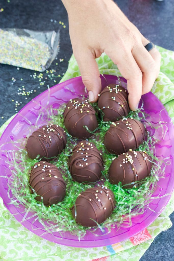 A hand picking up a chocolate egg from a purple egg tray with green easter grass. 