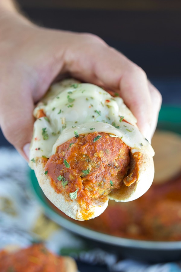 A close up shot of a hand holding a meatless sub topped with melted cheese.