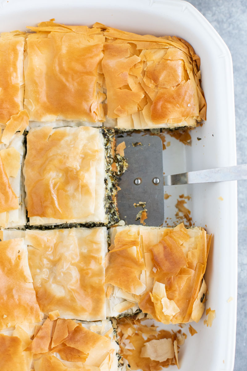 A white casserole dish filled with vegan spanakopita and a spatula. 