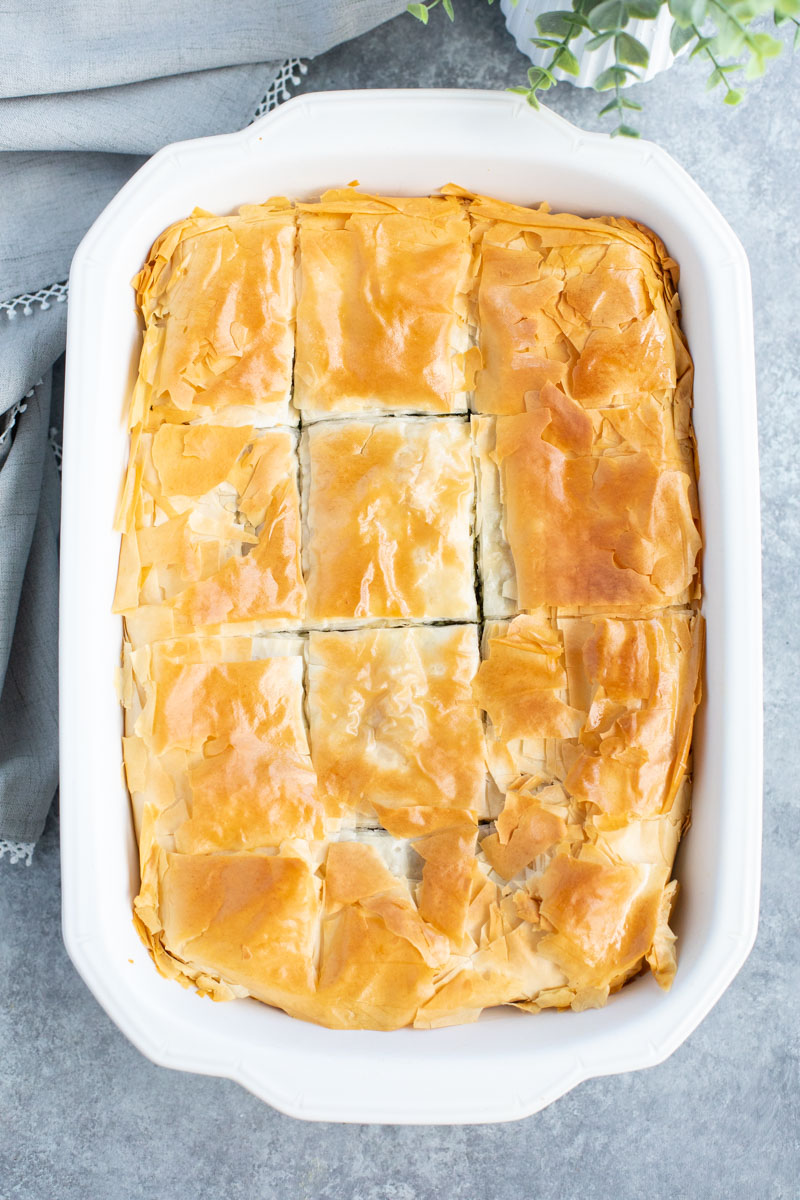 Overhead view of a white casserole dish of vegan spanakopita on a gray background.