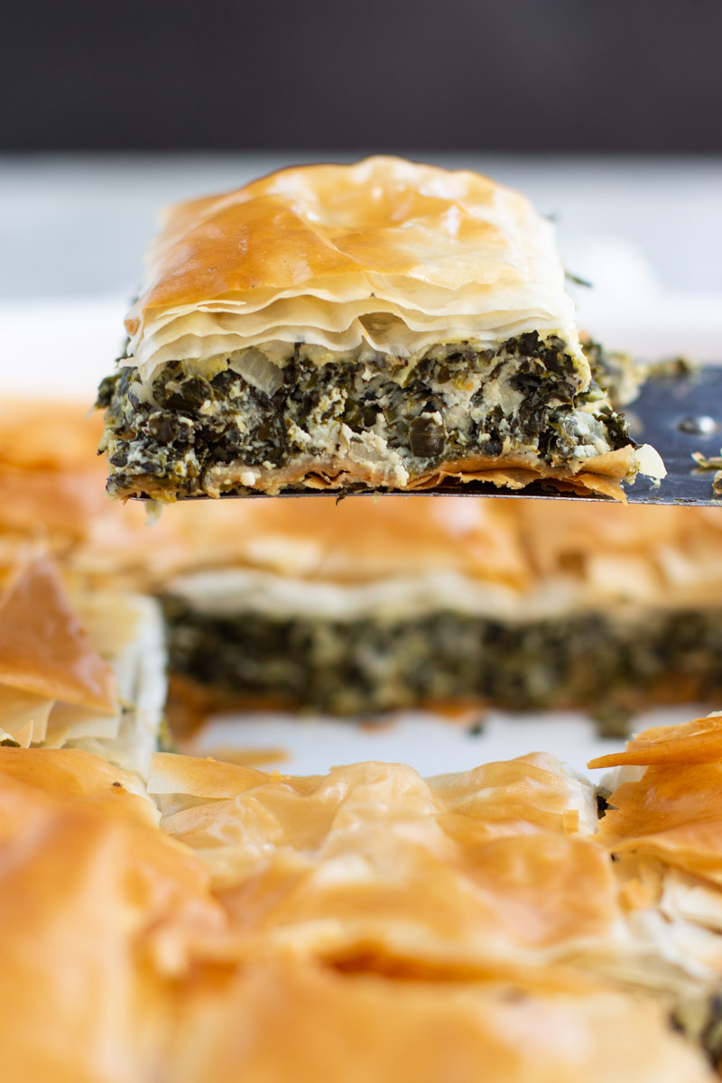 A spatula holding a slice of vegan spanakopita over the rest of the pie. 