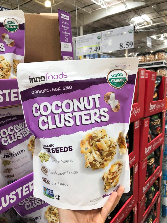 A hand holding a bag of organic vegan coconut clusters for $8.59 at Costco.