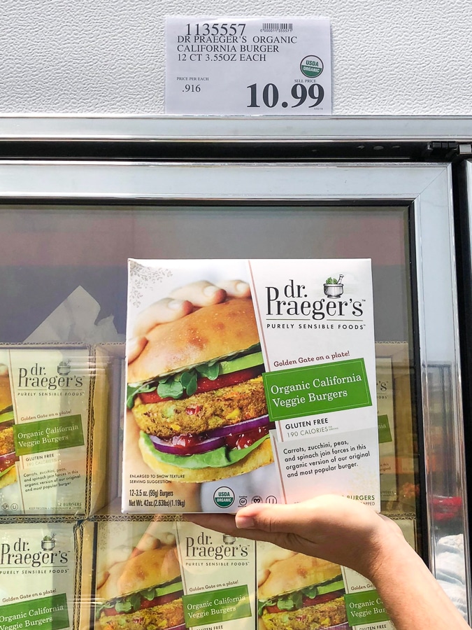 A hand holding a box of Dr. Praeger's organic vegan veggie burgers for $10.99 at Costco.