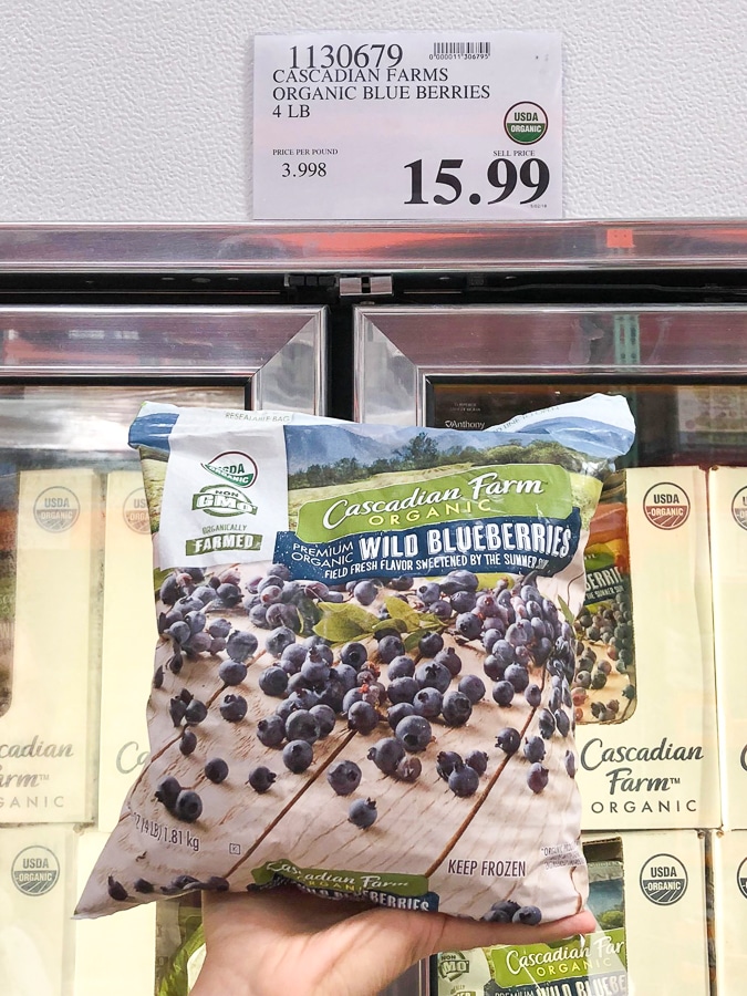 A hand holding a bag of organic frozen wild blueberries for $15.99 at Costco.