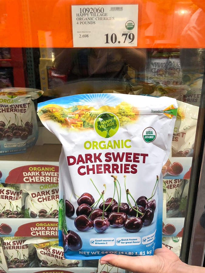 A hand holding a bag of frozen organic cherries for $10.79 at Costco.