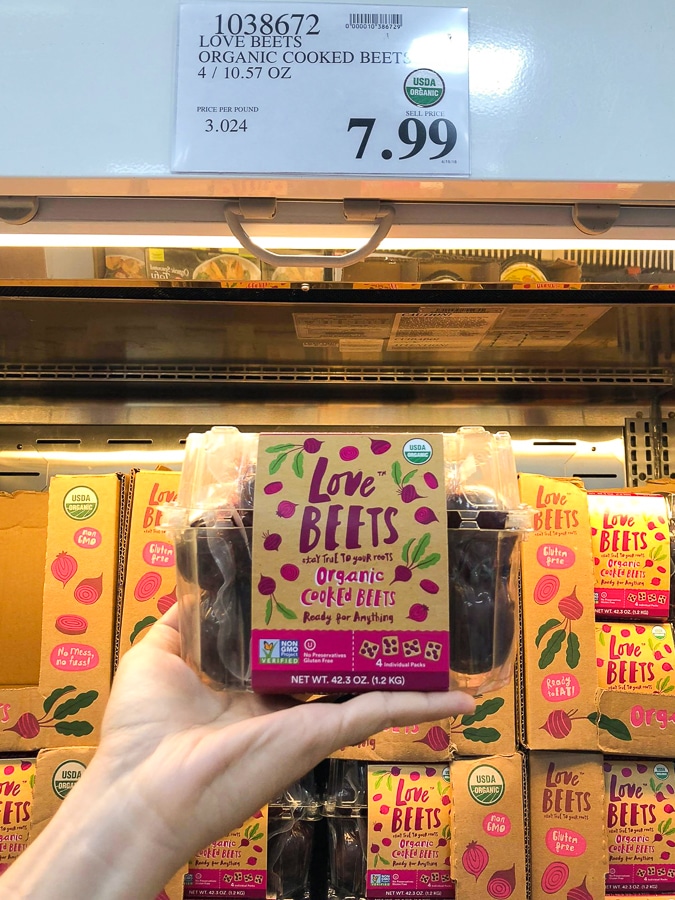 A hand holding a package of cooked beets in front of a price tag.