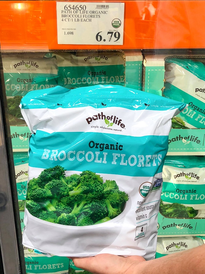 A hand holding a bag of organic frozen broccoli for $6.79 at Costco.