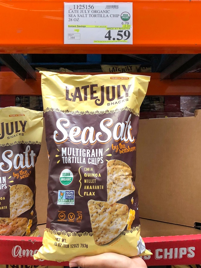 A hand holding a large bag of organic vegan Late July multigrain tortilla chips for $4.59 at Costco.