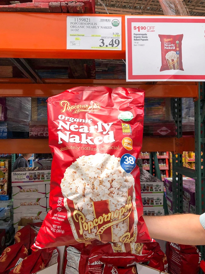 A hand holding a large red bag of organic vegan Popcornopolis popcorn for $3.49 at Costco.. 