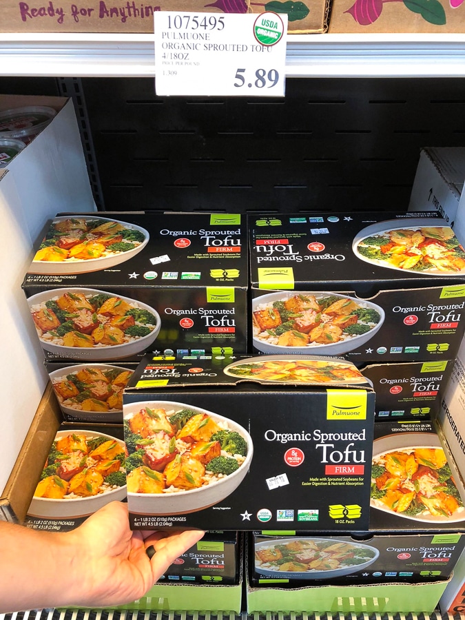 A hand holding a black box of organic vegan sprouted tofu for $5.89 a Costco.