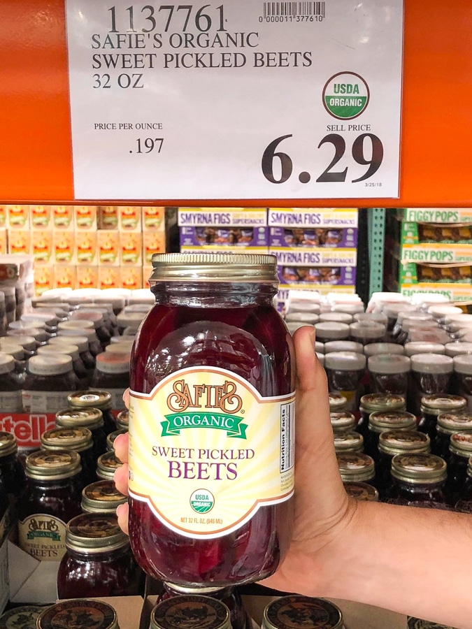 A hand holding a glass jar of organic vegan pickled beets for $6.29 at Costco.