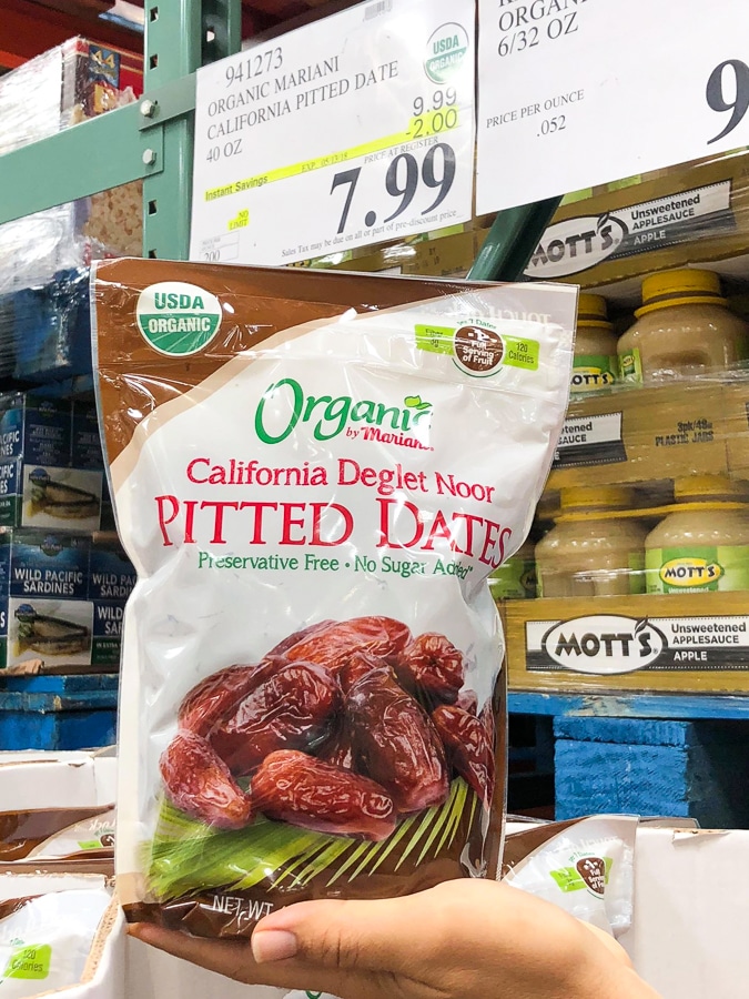 A hand holding a plastic bag of organic vegan Mariani California Deglet noon pitted dates for $7.99 at Costco. 