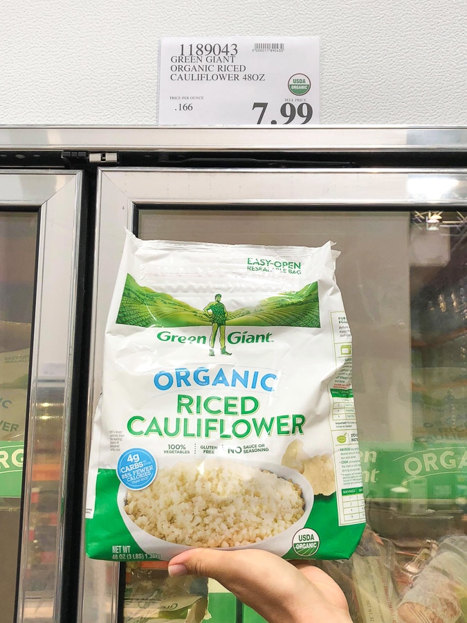 A hand holding a bag of frozen organic vegan riced cauliflower for $7.99 at Costco.