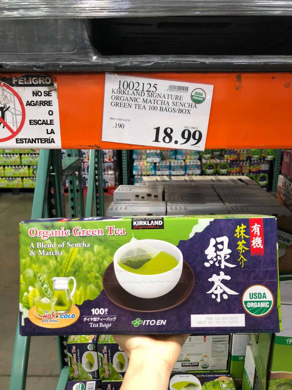 A hand holding a large box of organic green tea for $18.99 at Costco. 