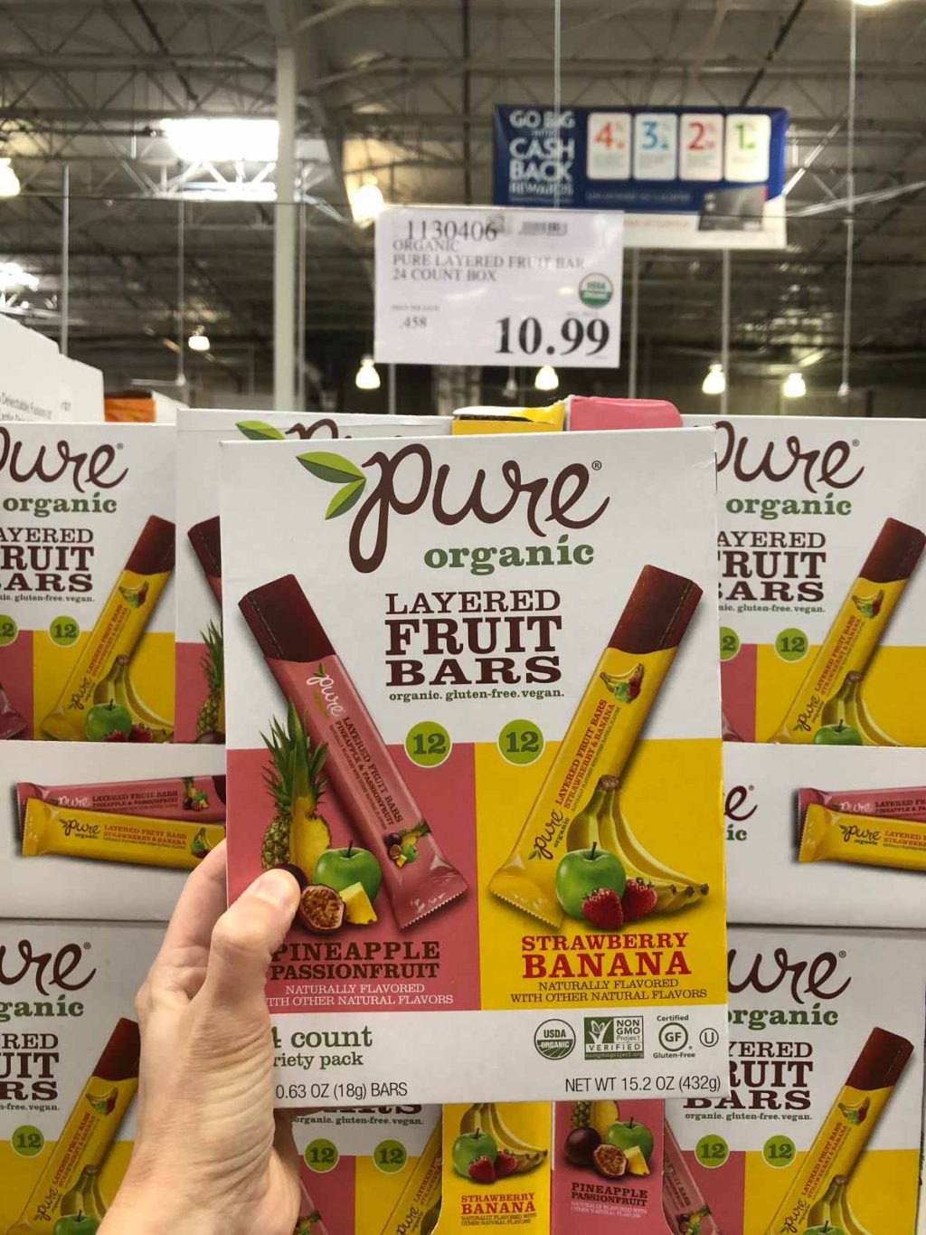 A hand holding a box of Pure organic vegan layered fruit bars for $10.99 at Costco.