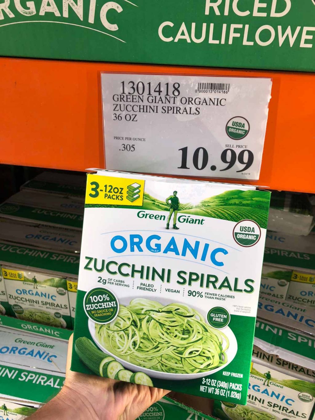 A hand holding a box of organic vegan frozen spirzelized zucchini noodles for $10.99 at Costco.