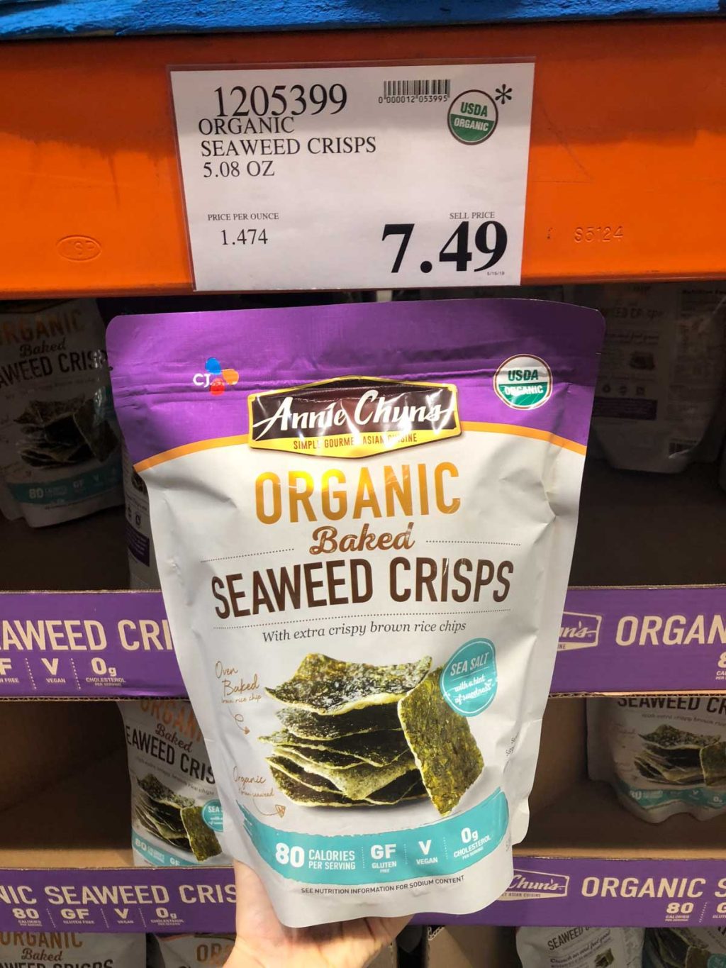 A hand holding a bag of organic baked seaweed crisps for $7.49 at Costco.