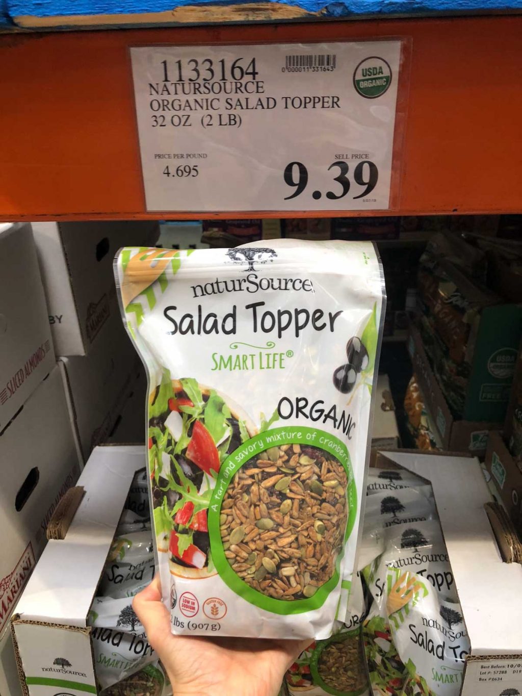 A hand holding a bag of organic vegan salad topper for $9.39 at Costco.