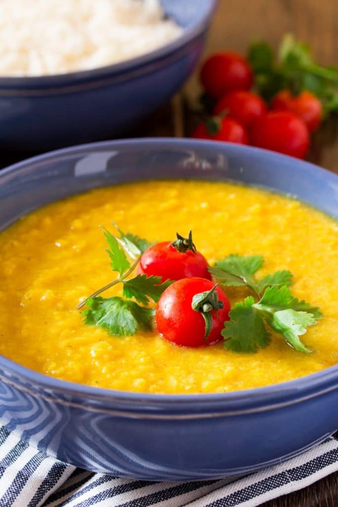 A blue bowl of red lentil soup with a tomato and cilantro garnish on top of a striped towel. 