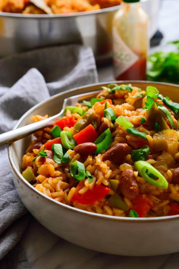 Vegan jumbalaya with beans and rice in a neutral colored bowl on a grey napkin. 