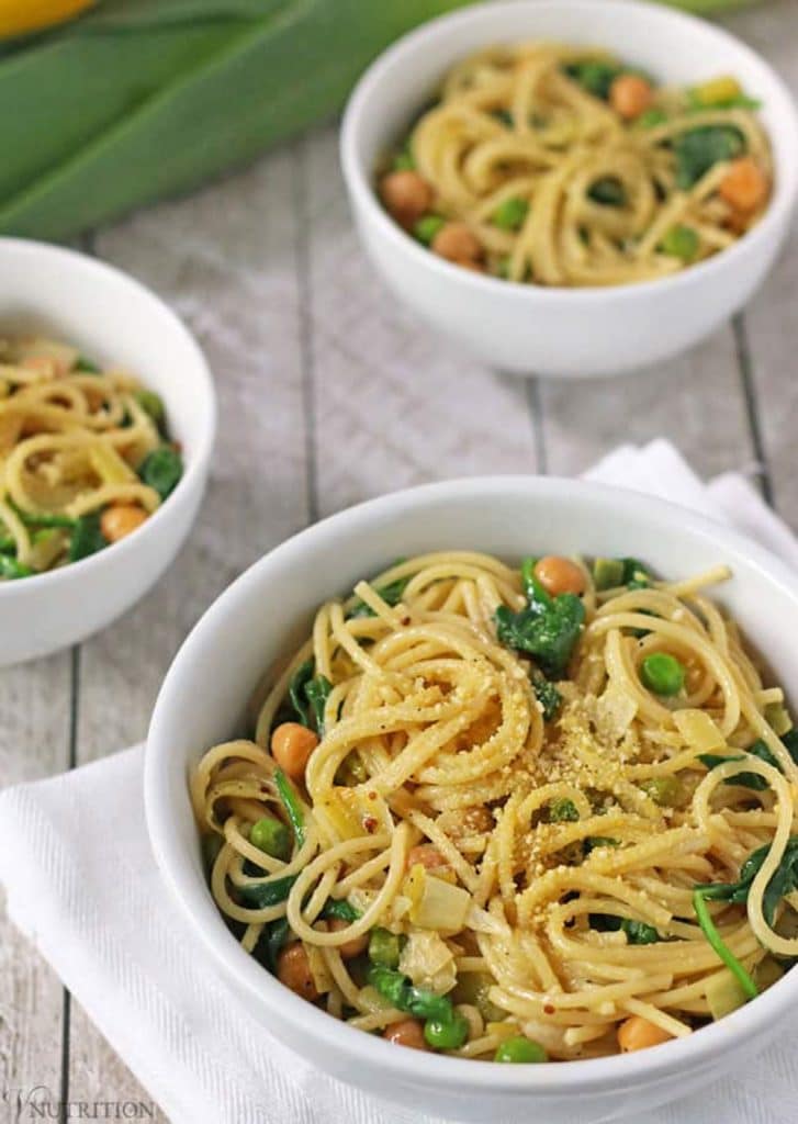 Three white bowls of lemon pasta with spinach and green peas on a grey background. 