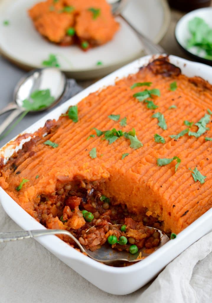 Vegan shepherd's pie topped with sweet potato mash in a white casserole dish on a light background. 