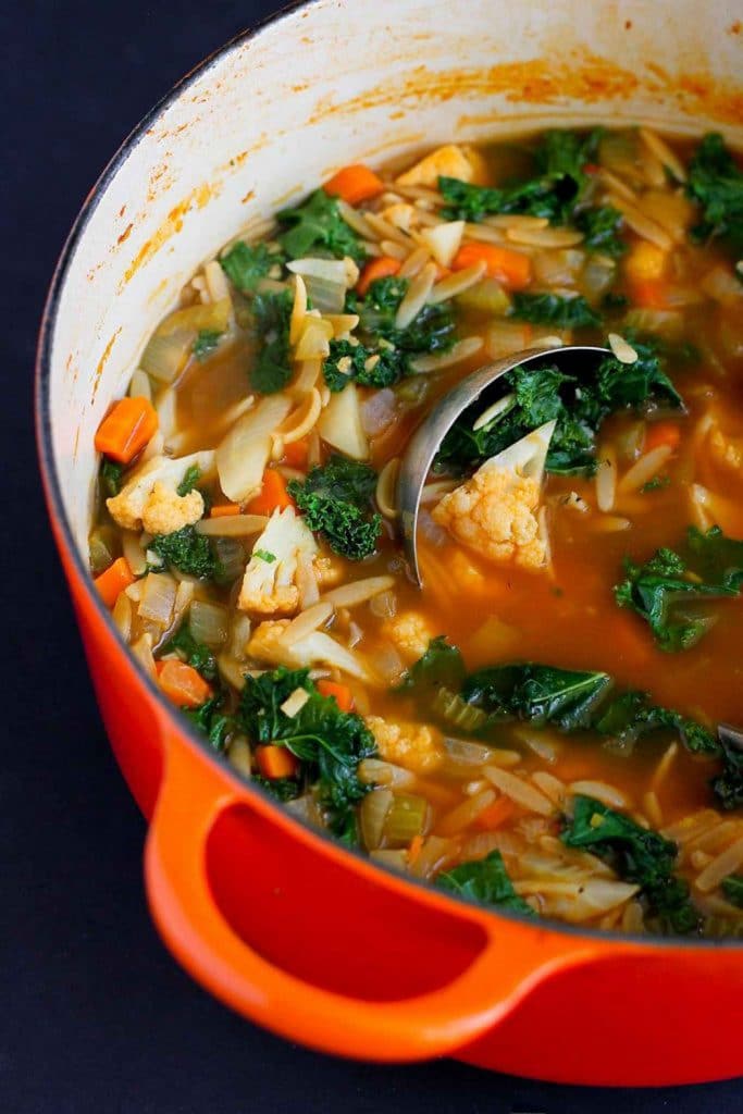 An orange dutch oven filled with kale cauliflower soup and a soup ladle. 