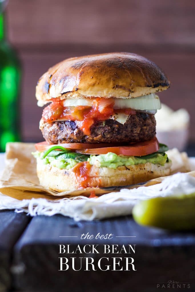 A loaded black bean burger on a fluffy roll that's resting on a picnic table. 