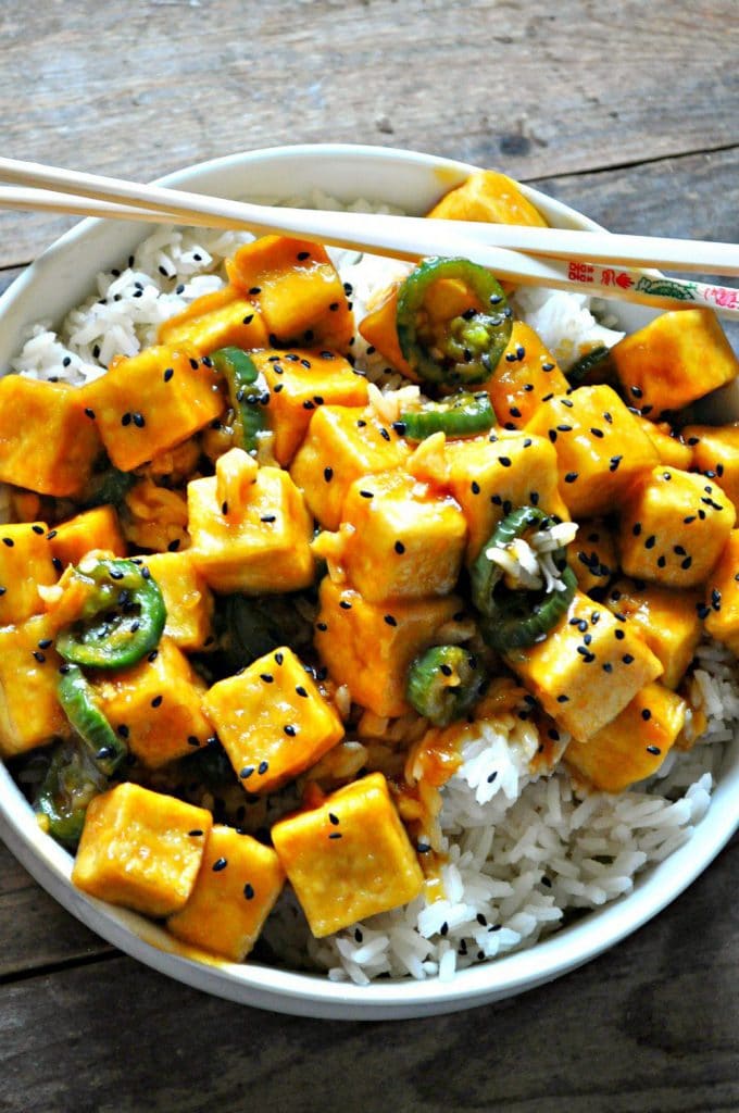 Crispy tofu tossed in garlic Hawaiian sauce over rice in a bowl with chopsticks. 