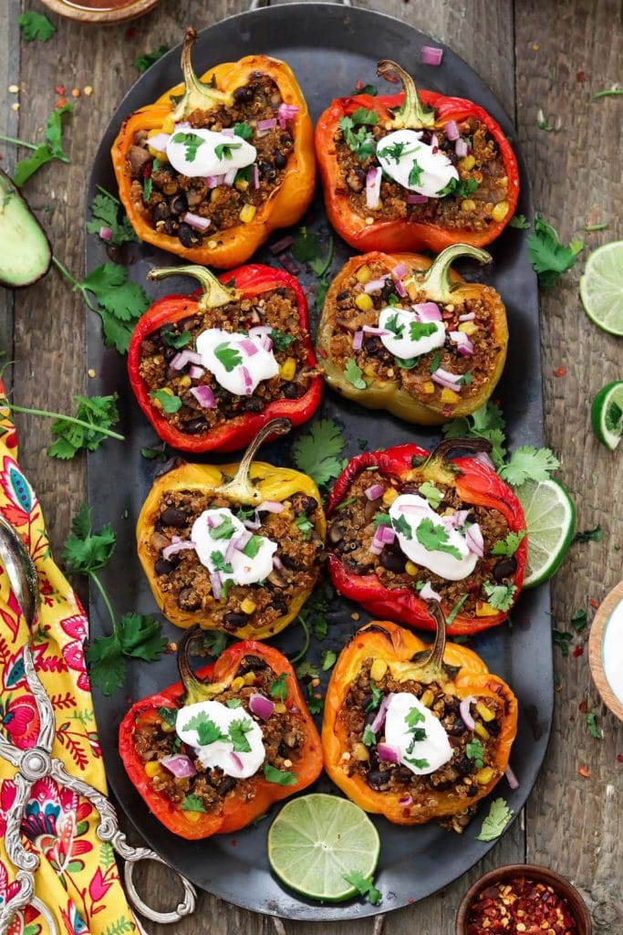 Vegan stuffed peppers topped with sour cream on a black platter on a rustic background.