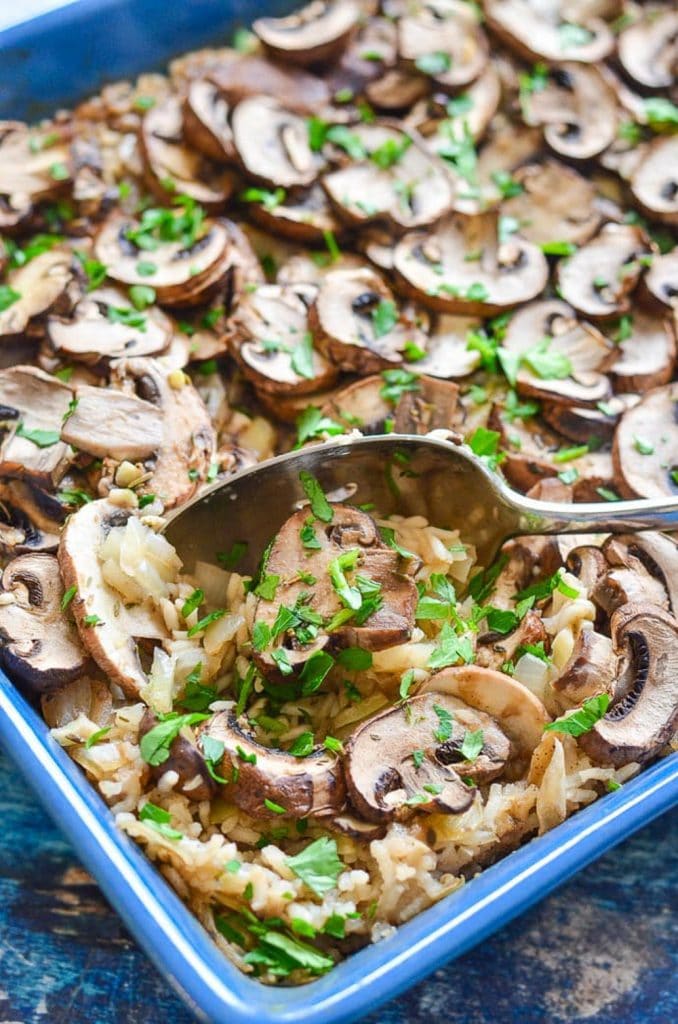 Mushroom and rice casserole in a blue casserole dish with a spoon scooping it out. 