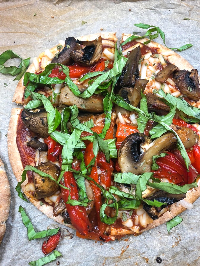 A closeup view of a vegetable pizza with fresh basil on a piece of parchment. 