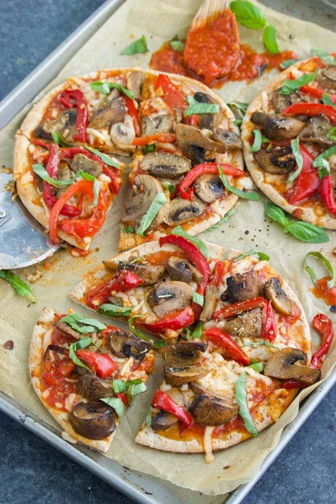 Three pita pizzas on a parchment lined tray on a dark background.