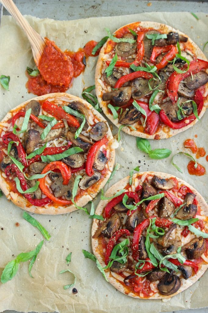 Three pizzas on top of a piece of parchment paper next to a wooden spoon.