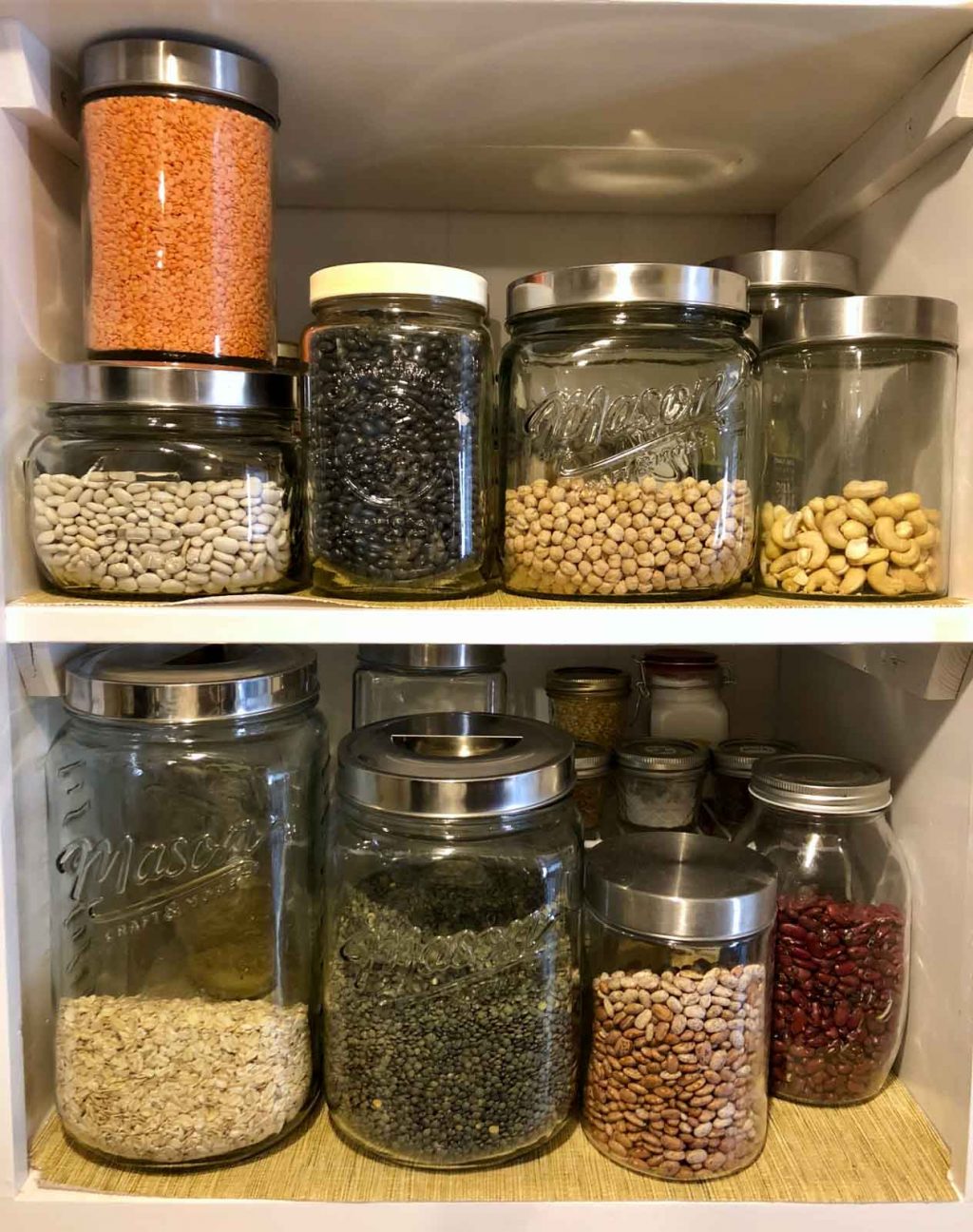 Two shelves of vegan products in glass jars (beans, lentils, oats) of a cheap vegan pantry.