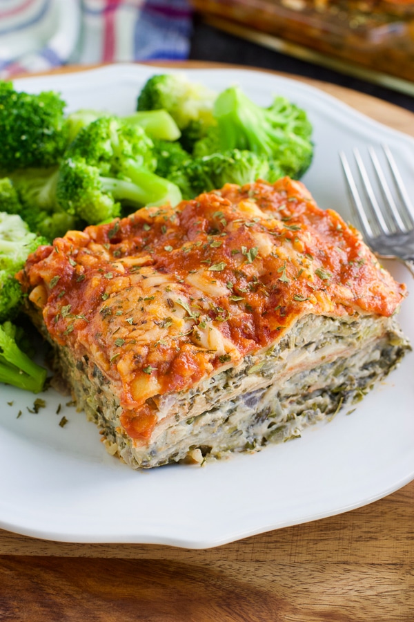 A piece of lasagna next to broccoli on a white plate on a rustic background.