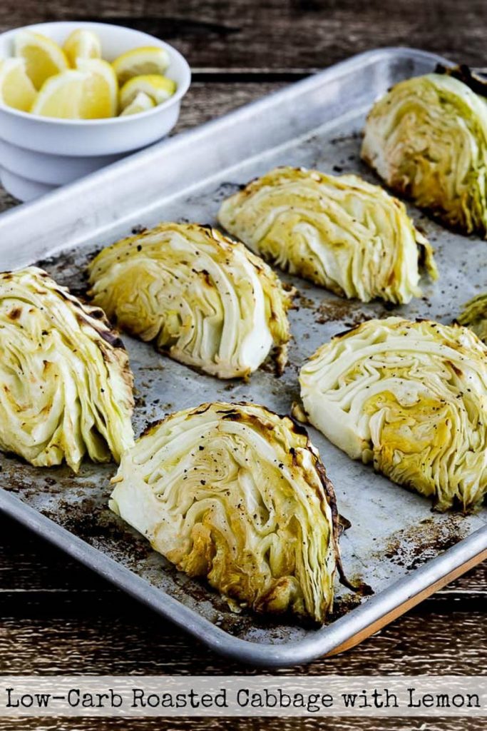 Low-carb vegan keto side dish of lemon roasted cabbage slices on a baking tray with a bowl of lemons on the side.