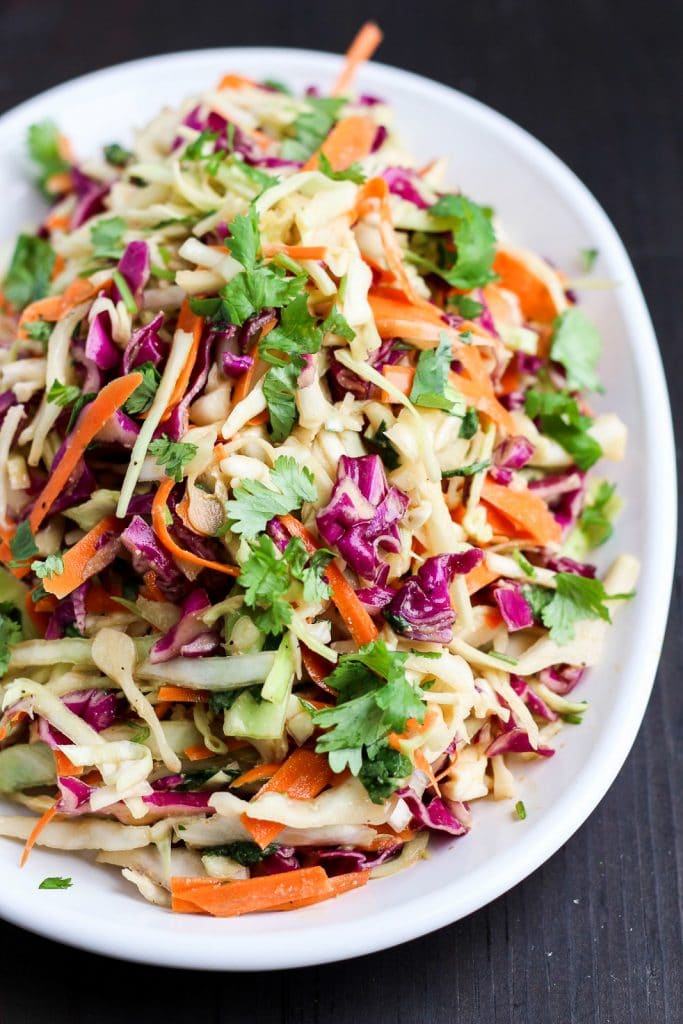 A vegan keto side dish of asian coleslaw is served on a large white platter and it's resting on a black background.