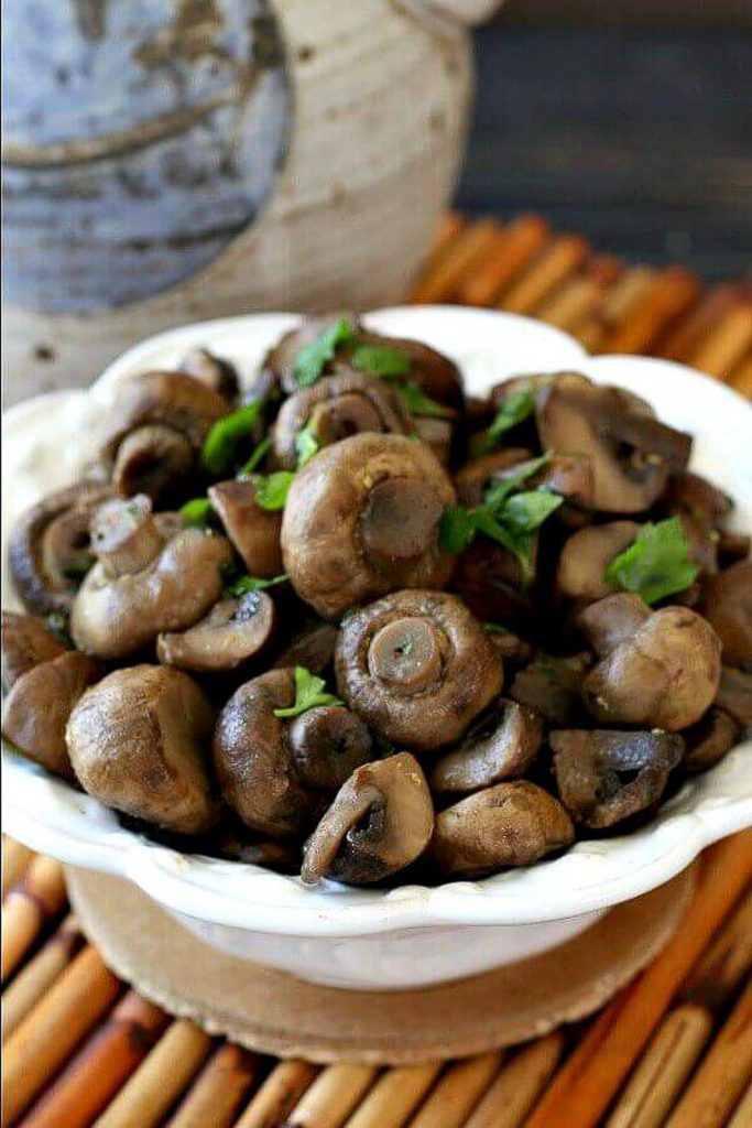 Vegan keto slow cooker balsamic mushrooms with parsley on top in a white bowl that is sitting on a wooden textured background.