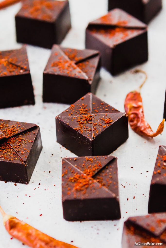 Multiple squares of vegan keto chocolate dessert with peppers on the side on top of a white background.