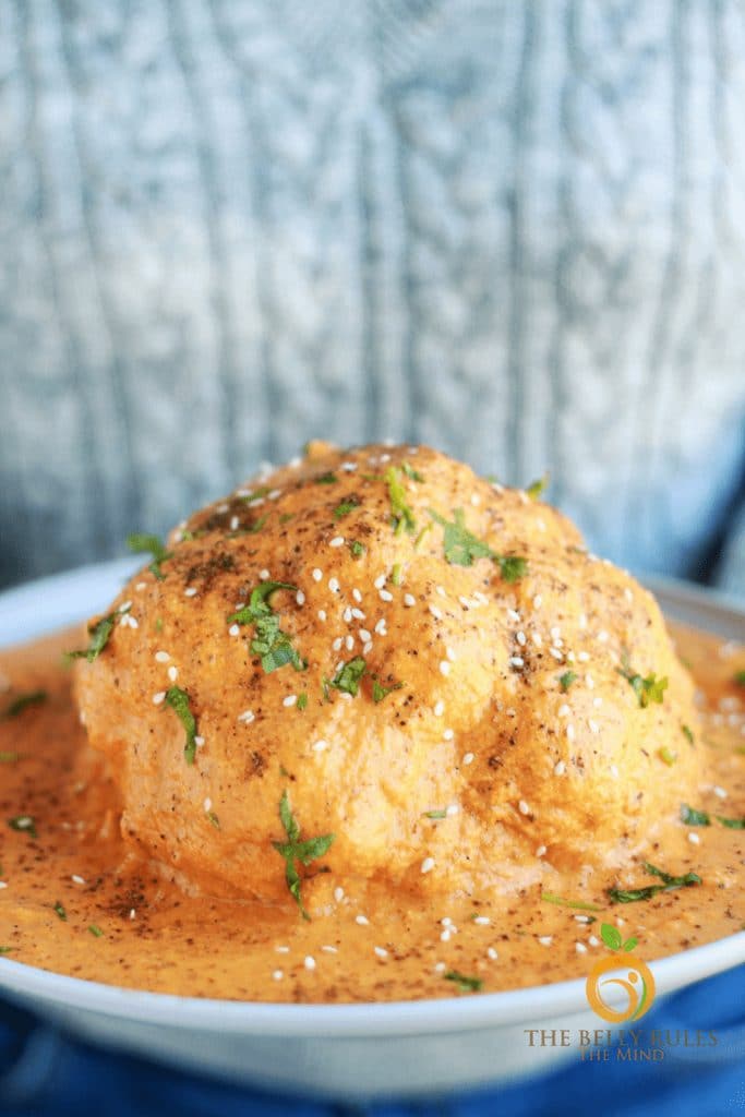 Instant pot Indian Masala-seasoned cauliflower head in a large bowl with lots of sauce that a person is holding.