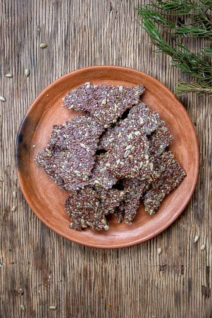A pile of seeded low-carb keto crackers on a brown plate that is placed on a rustic background.