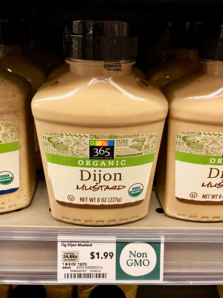 Multiple bottles of organic dijon mustard on a shelf at Whole Foods. 